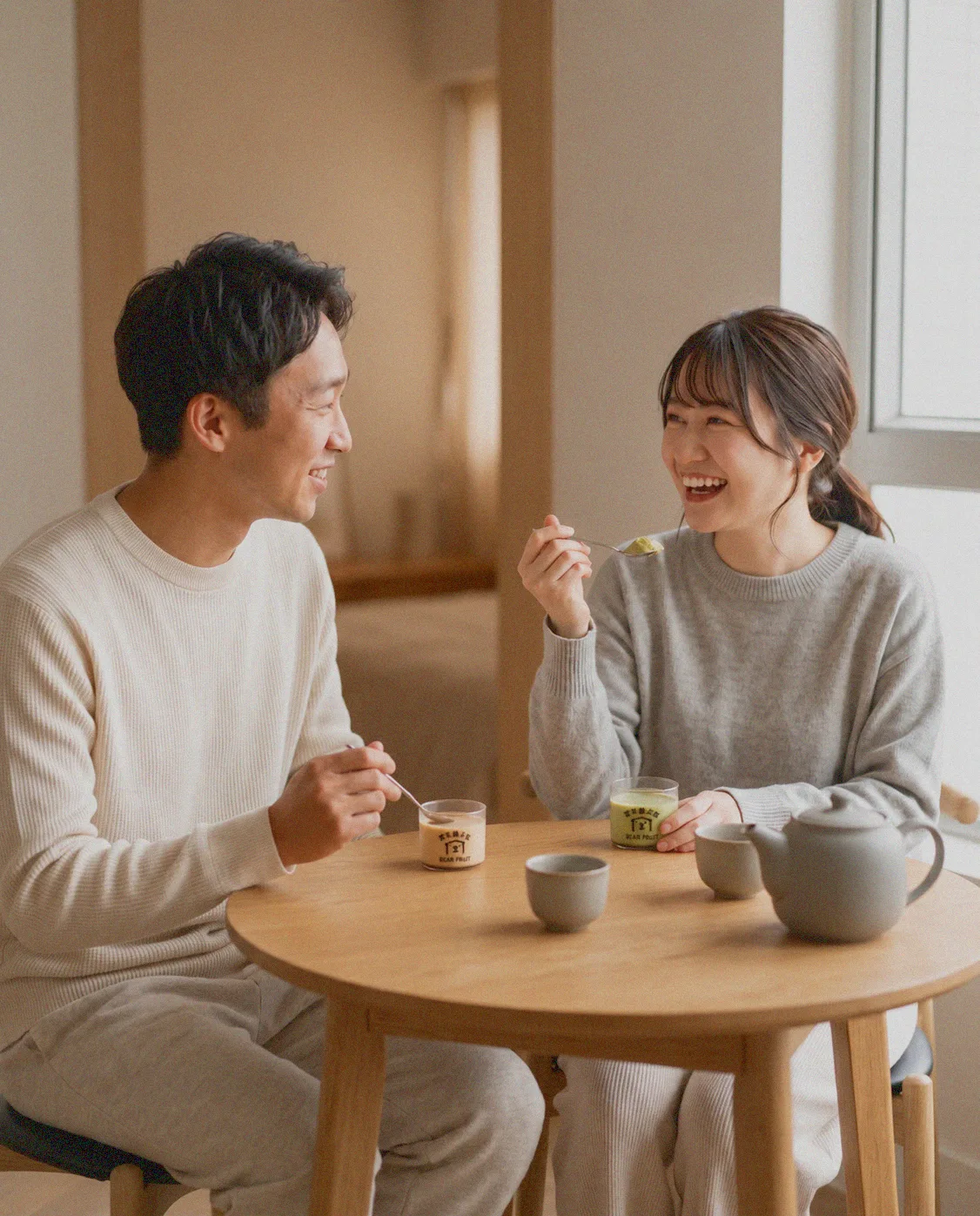 Two people laughing over Bear Fruit puddings and tea at a round wooden table
